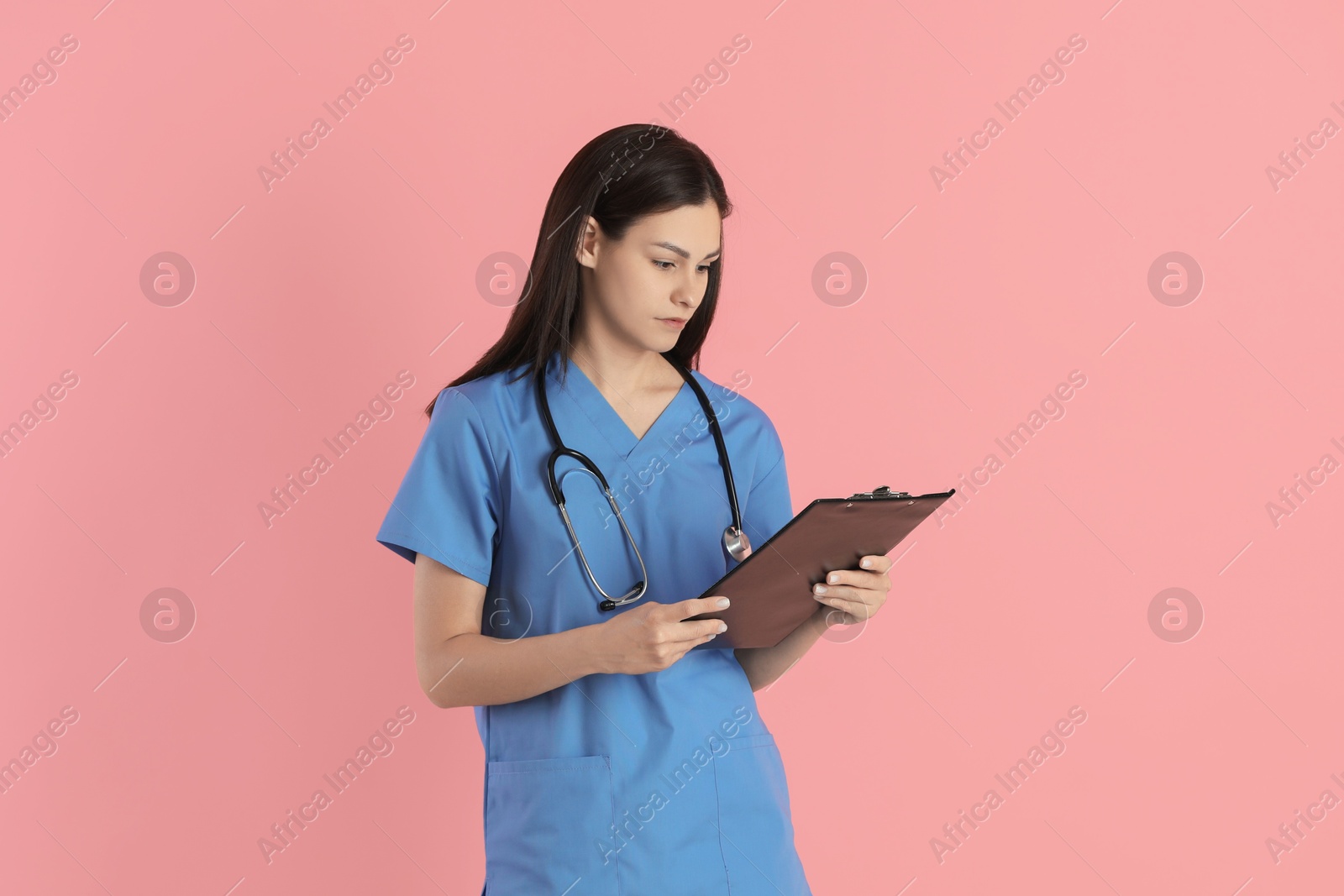 Photo of Beautiful nurse with clipboard on pink background