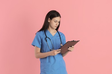 Photo of Beautiful nurse with clipboard on pink background