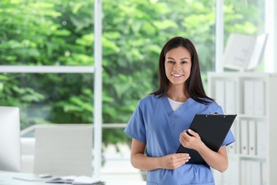 Smiling nurse with clipboard in hospital office. Space for text