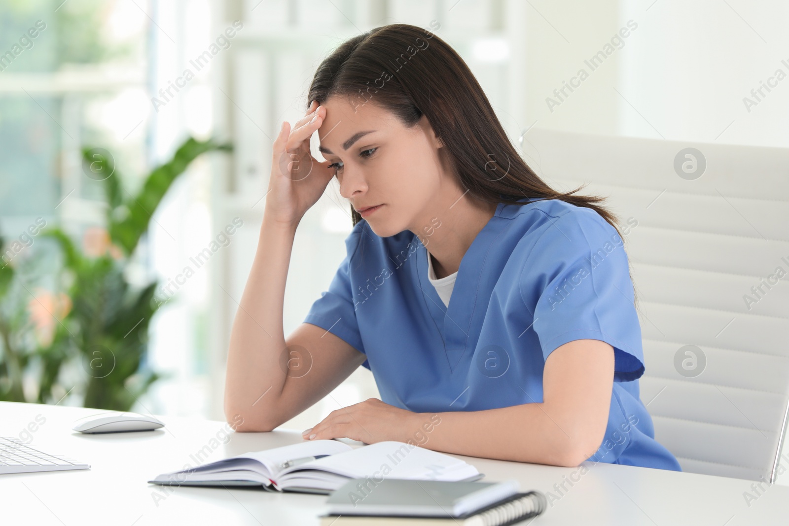 Photo of Tired nurse at table in hospital office