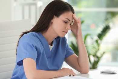 Photo of Tired nurse at table in hospital office