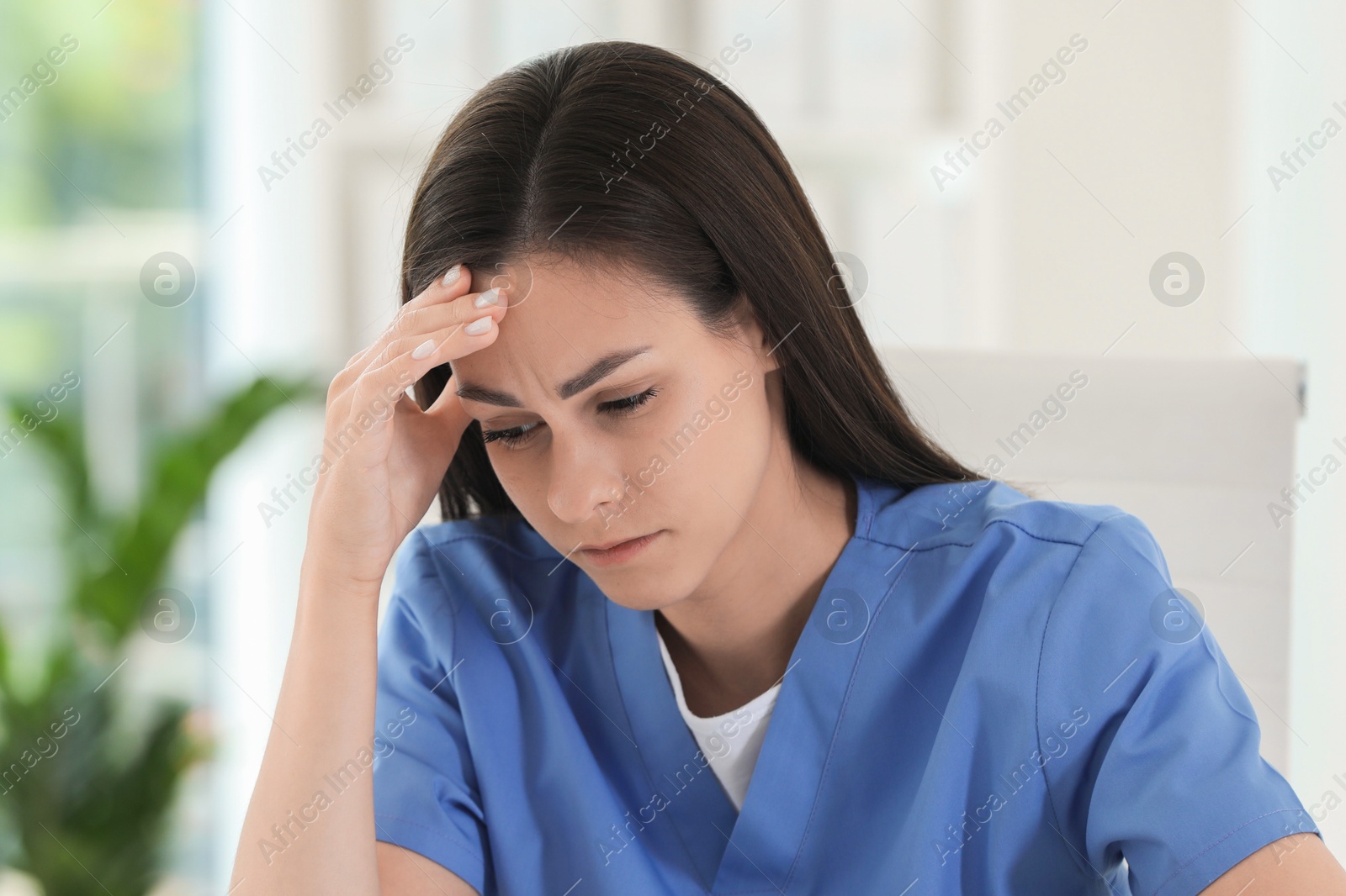 Photo of Tired nurse suffering from headache in hospital office