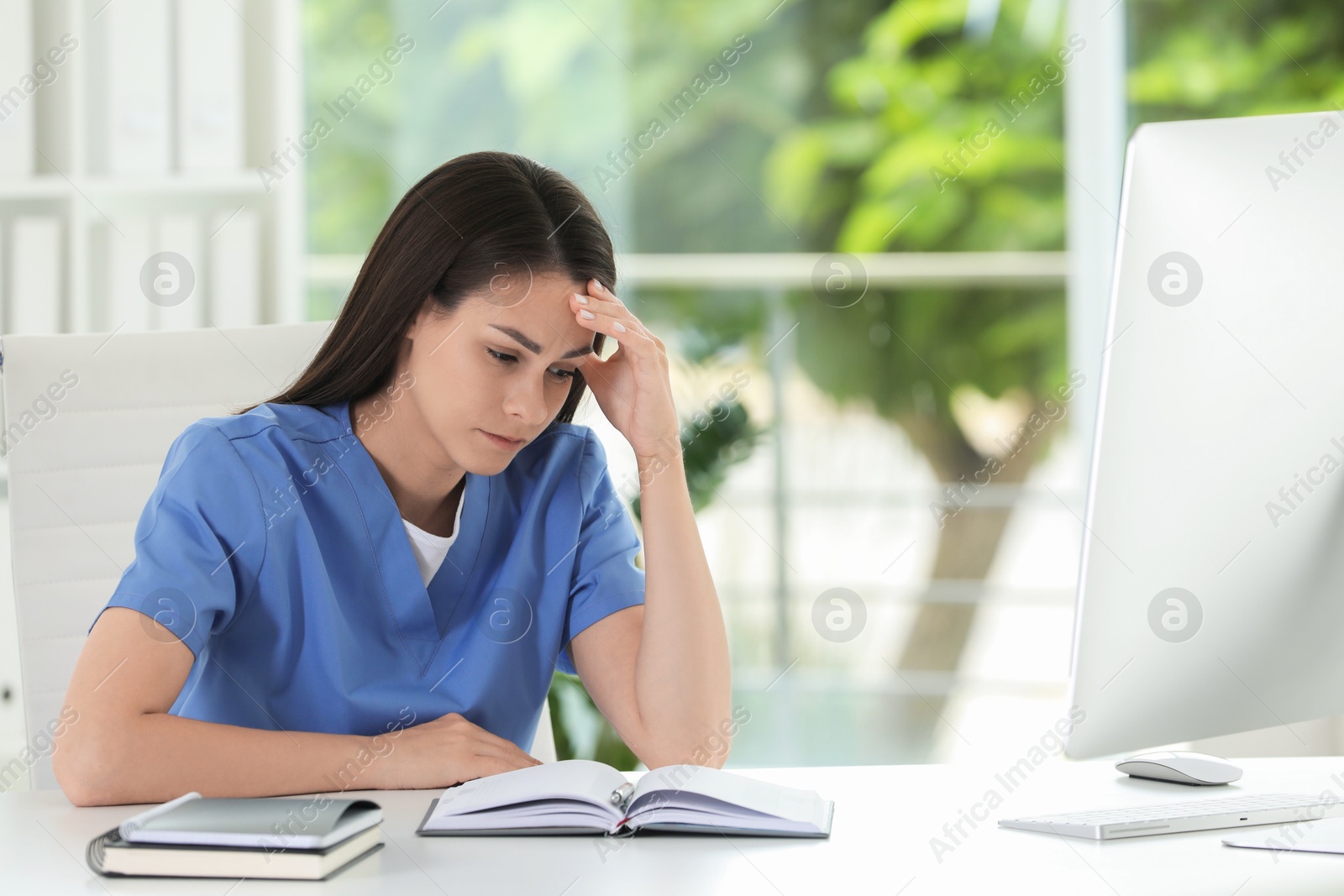 Photo of Tired nurse at table in hospital office