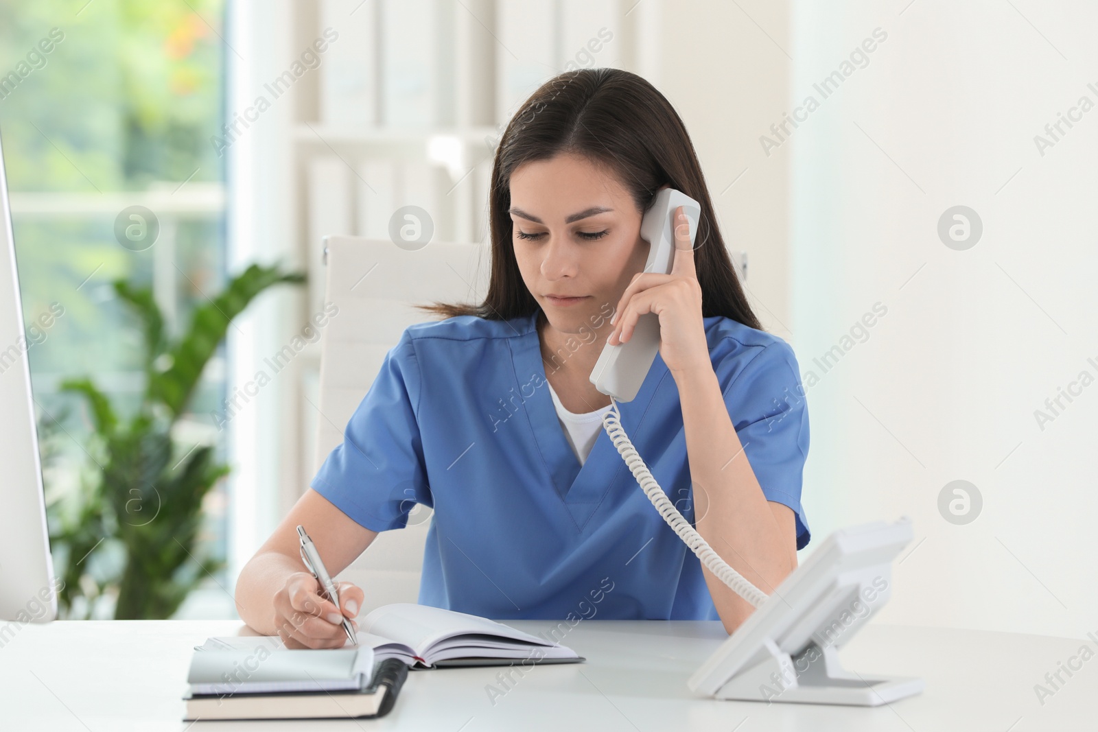 Photo of Beautiful nurse working with clients by telephone at table in hospital office