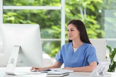 Photo of Beautiful nurse working with computer at table in hospital office