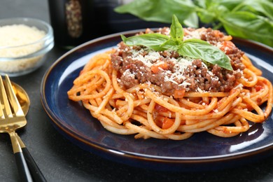 Photo of Delicious pasta bolognese with basil served on black table, closeup