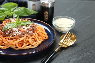 Photo of Delicious pasta bolognese with basil served on black table, closeup