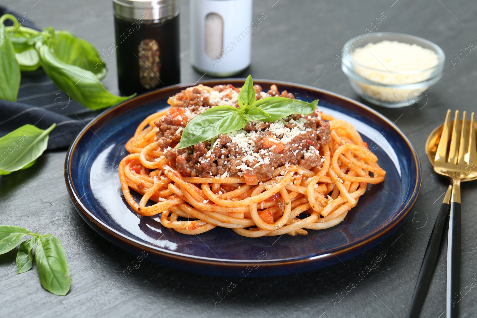 Photo of Delicious pasta bolognese with basil served on black table, closeup