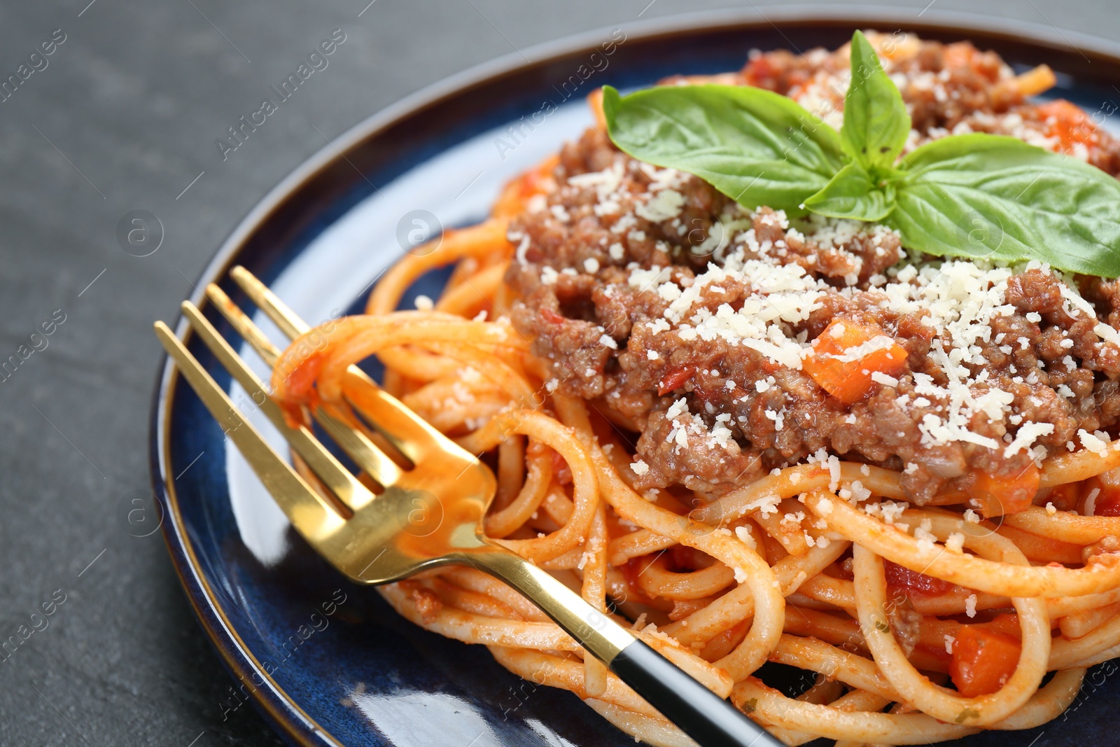 Photo of Delicious pasta bolognese with basil on black table, closeup