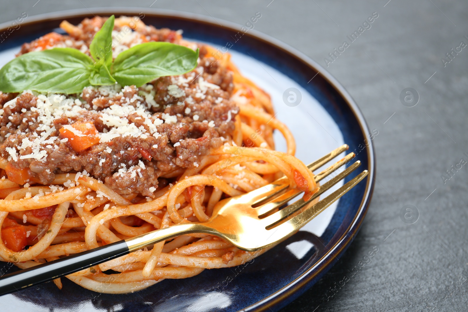 Photo of Delicious pasta bolognese with basil on black table, closeup