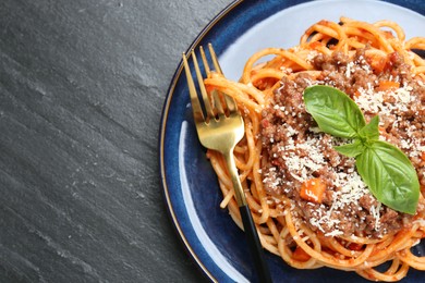 Photo of Delicious pasta bolognese with basil and fork on black table, top view. Space for text