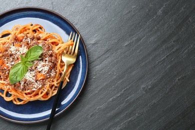 Photo of Delicious pasta bolognese with basil and fork on black table, top view. Space for text