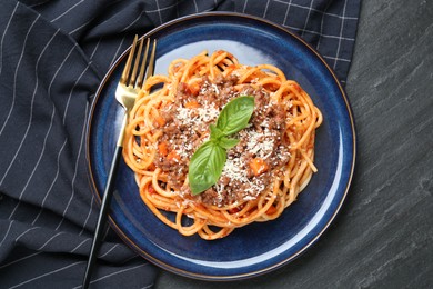 Photo of Delicious pasta bolognese with basil and fork on black table, top view