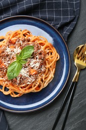 Photo of Delicious pasta bolognese with basil served on black table, top view