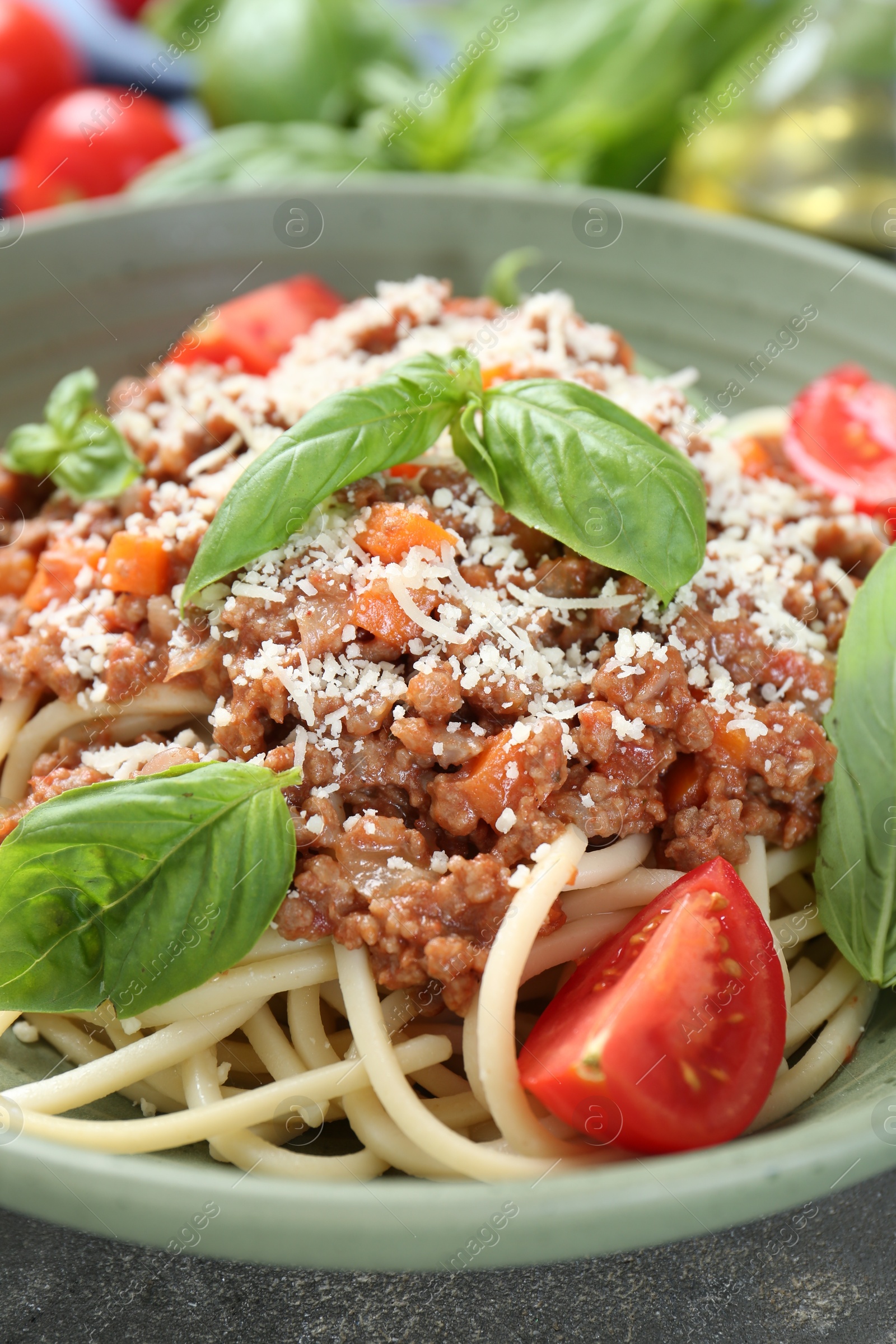 Photo of Delicious pasta bolognese with basil and tomatoes on grey table, closeup