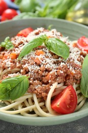 Photo of Delicious pasta bolognese with basil and tomatoes on grey table, closeup