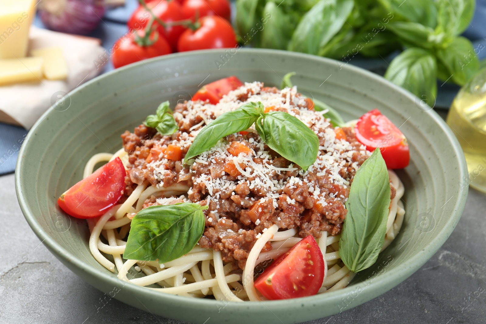 Photo of Delicious pasta bolognese with basil and tomatoes on grey table, closeup