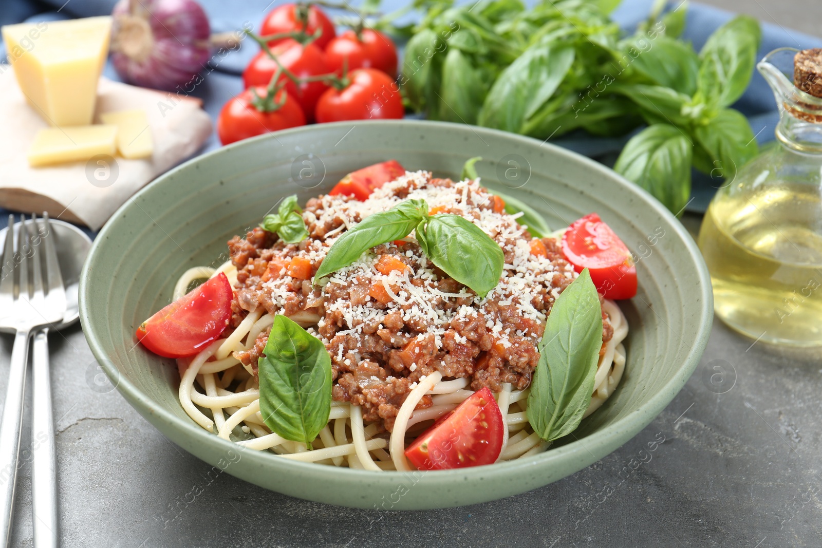 Photo of Delicious pasta bolognese with basil and tomatoes served on grey table, closeup