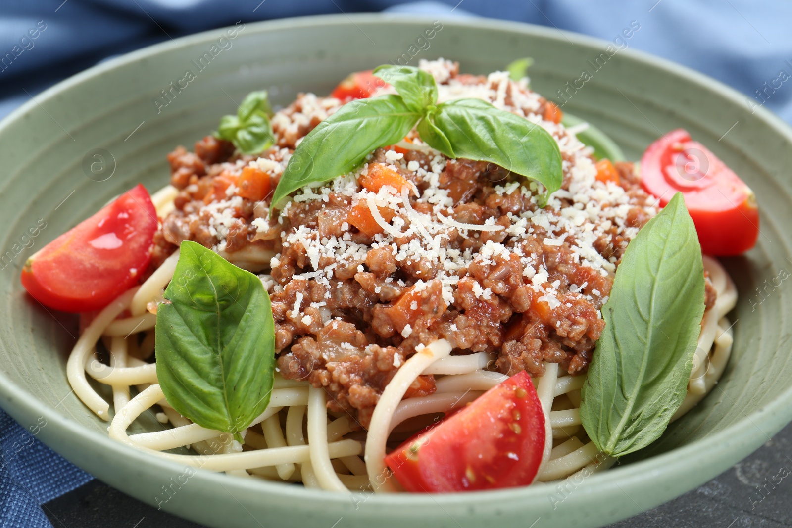 Photo of Delicious pasta bolognese with basil and tomatoes on grey table, closeup