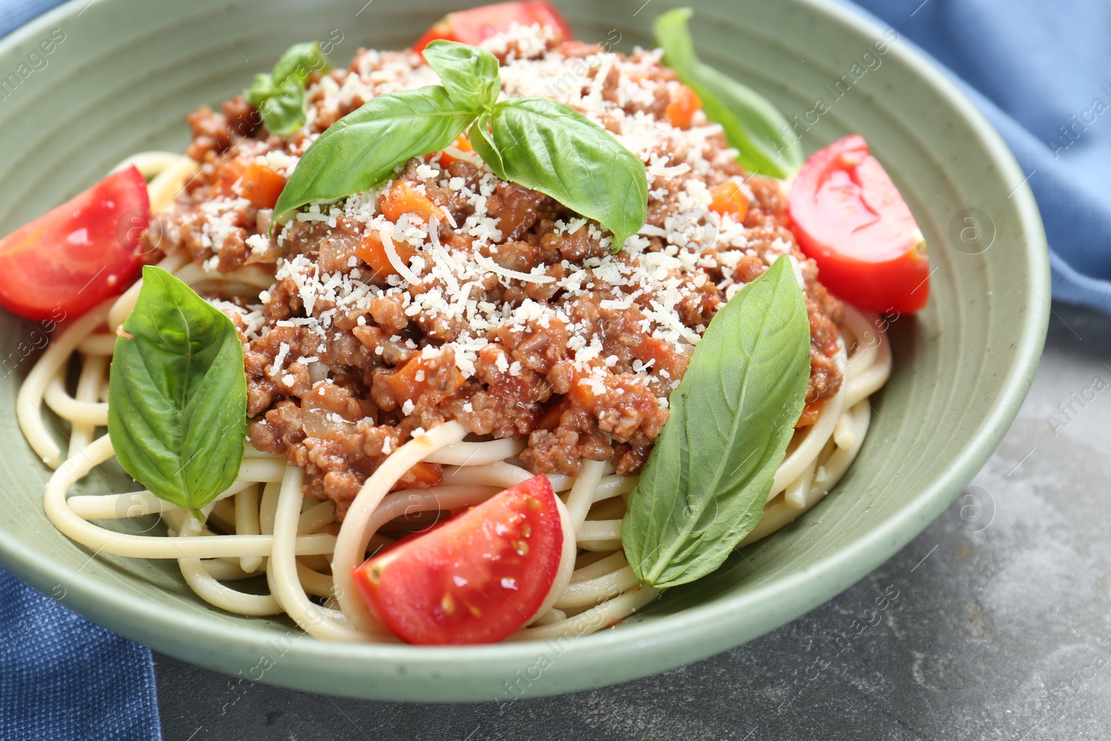 Photo of Delicious pasta bolognese with basil and tomatoes on grey table, closeup