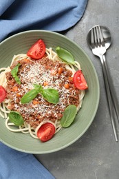 Photo of Delicious pasta bolognese with basil and tomatoes served on grey table, top view