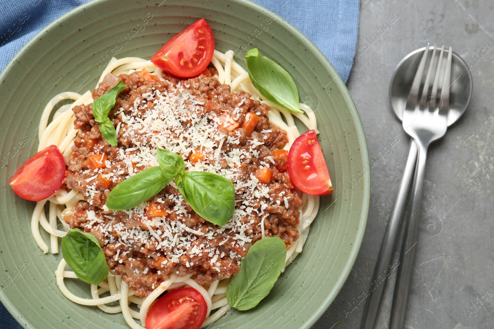 Photo of Delicious pasta bolognese with basil and tomatoes served on grey table, top view