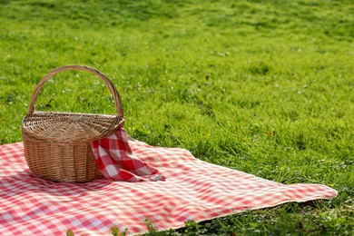 Photo of One picnic wicker basket with checkered napkin and blanket on green grass. Space for text