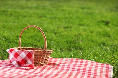 Photo of One picnic wicker basket with checkered napkin and blanket on green grass. Space for text