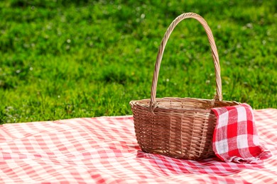 Photo of One picnic wicker basket with checkered napkin and blanket on green grass. Space for text