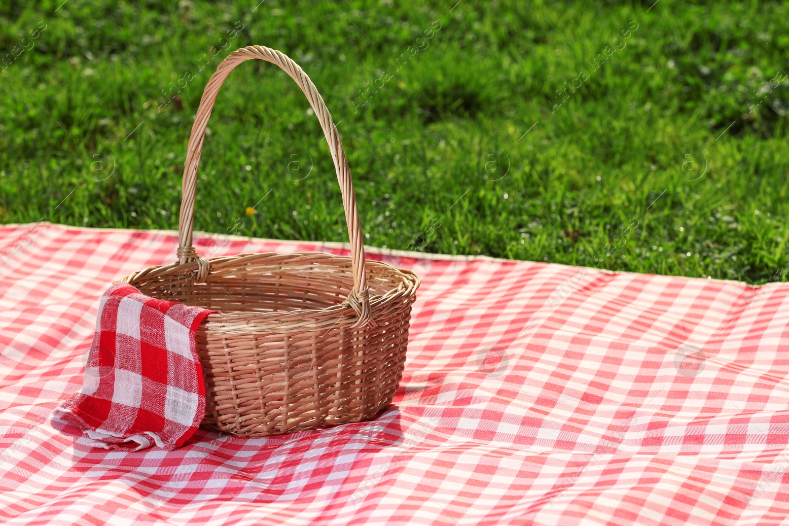 Photo of One picnic wicker basket with checkered napkin and blanket on green grass. Space for text