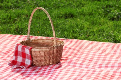 Photo of One picnic wicker basket with checkered napkin and blanket on green grass. Space for text