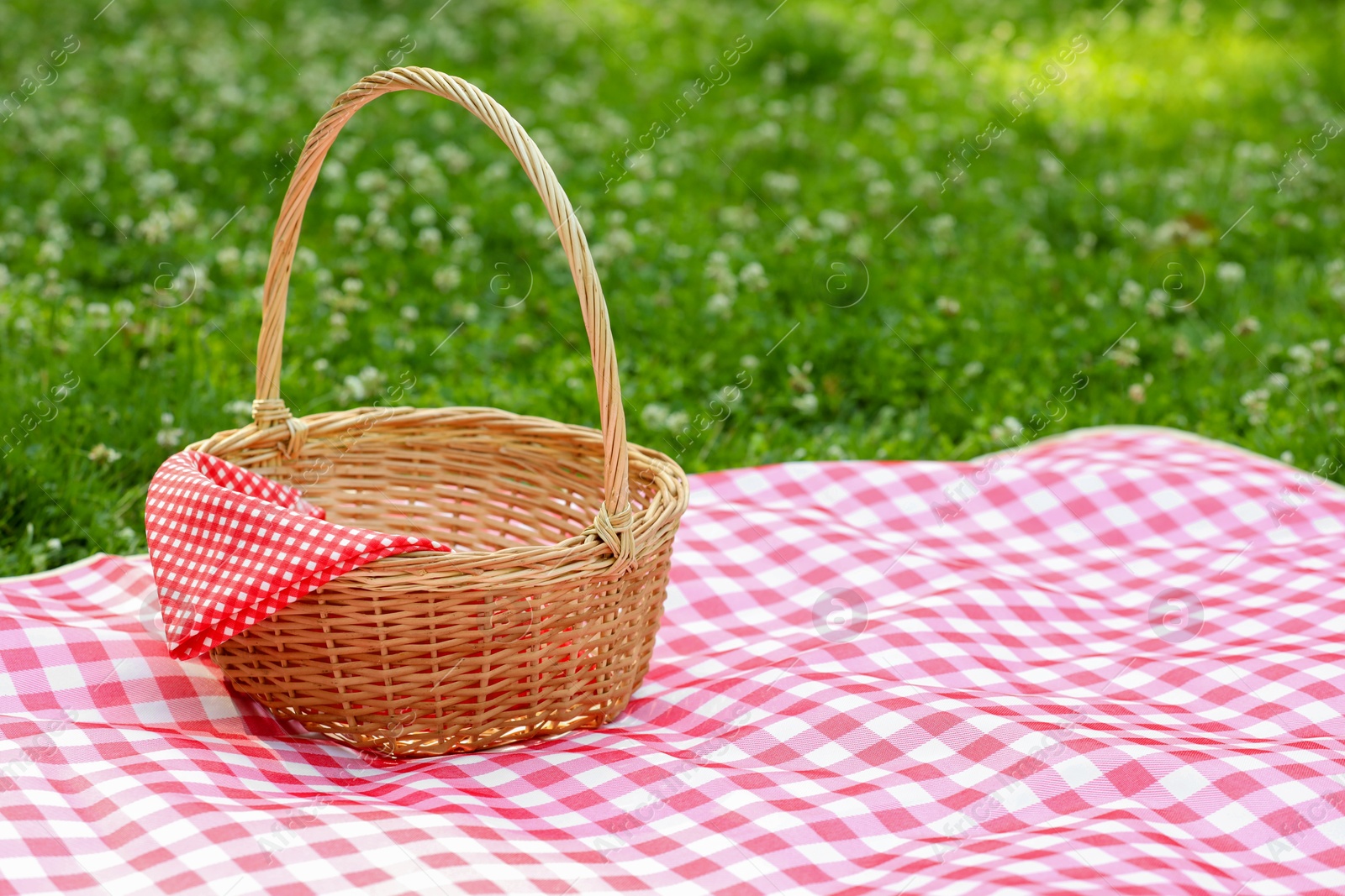 Photo of One picnic wicker basket with checkered napkin and blanket on green grass. Space for text