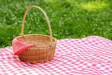 Photo of One picnic wicker basket with checkered napkin and blanket on green grass. Space for text