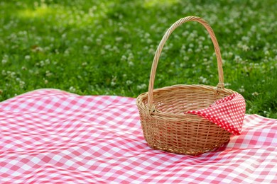 Photo of One picnic wicker basket with checkered napkin and blanket on green grass. Space for text