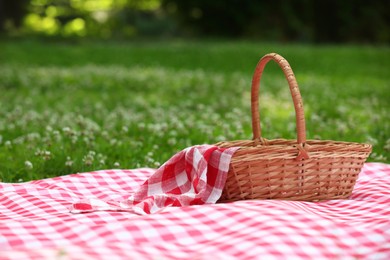 Photo of One picnic wicker basket with checkered napkin and blanket on green grass. Space for text