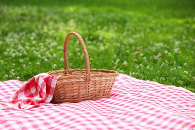 Photo of One picnic wicker basket with checkered napkin and blanket on green grass. Space for text