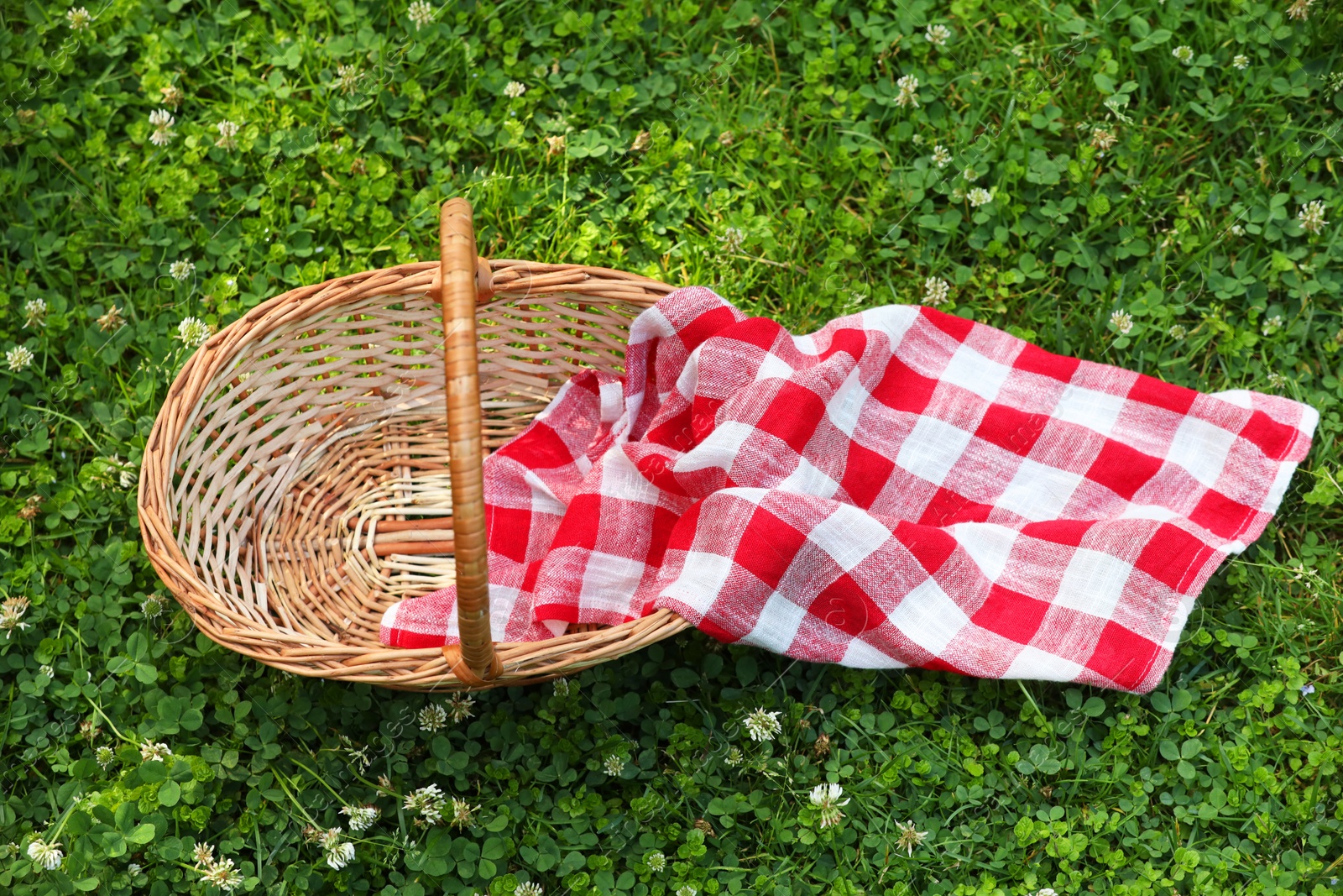 Photo of One picnic wicker basket with checkered napkin on green grass, above view