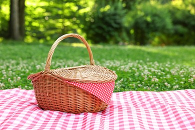 Photo of One picnic wicker basket with checkered napkin and blanket on green grass. Space for text