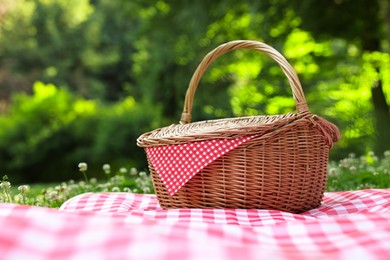 Photo of One picnic wicker basket with checkered napkin and blanket on green grass. Space for text