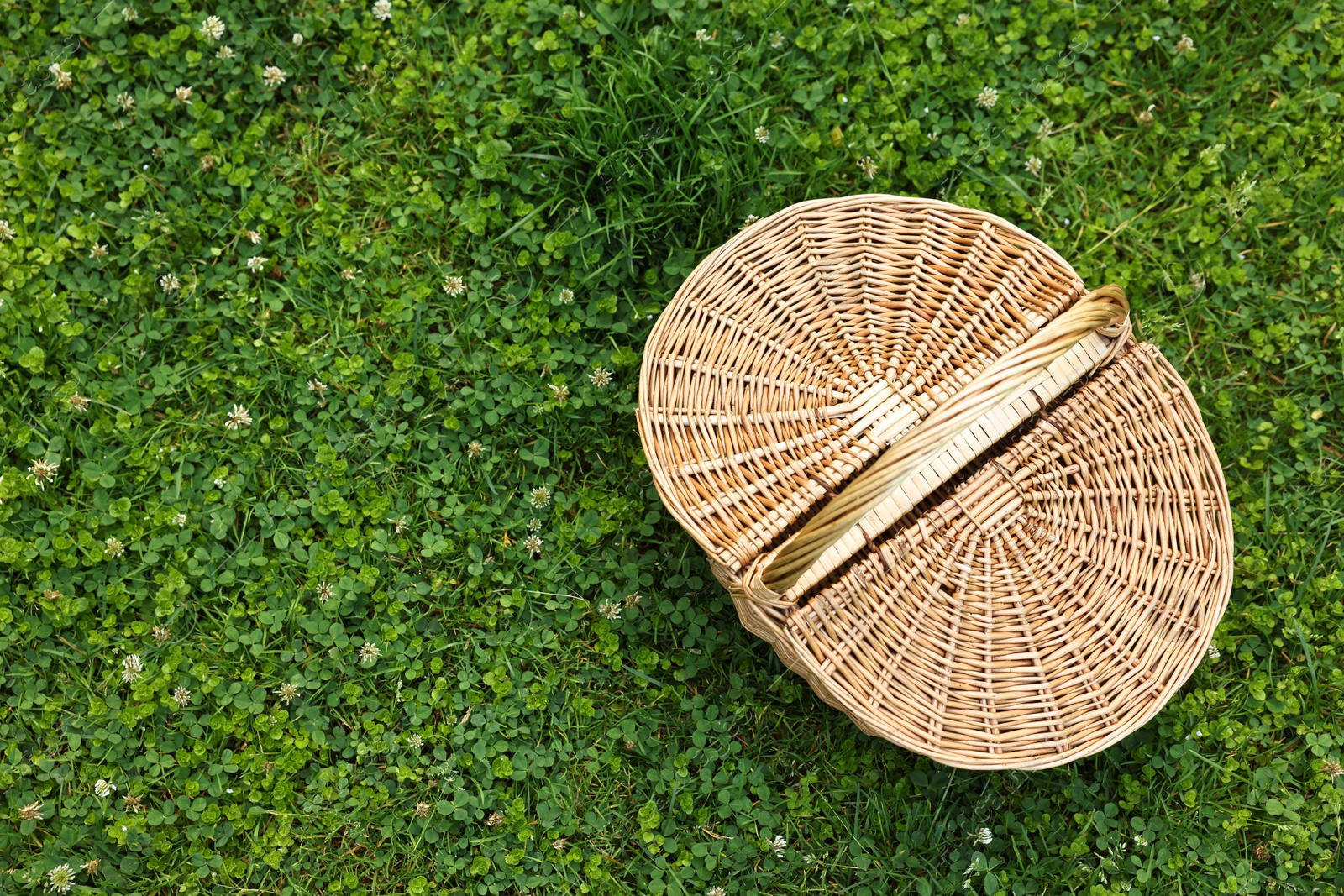 Photo of One picnic wicker basket on green grass, top view. Space for text