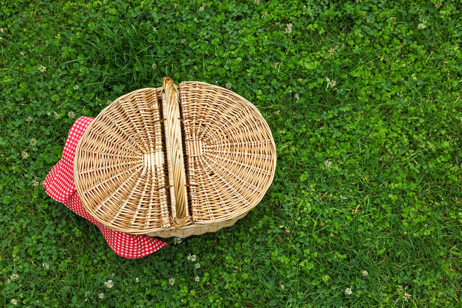 Photo of One picnic wicker basket with checkered napkin on green grass, above view. Space for text