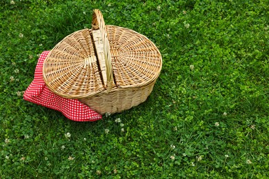 Photo of One picnic wicker basket with checkered napkin on green grass. Space for text