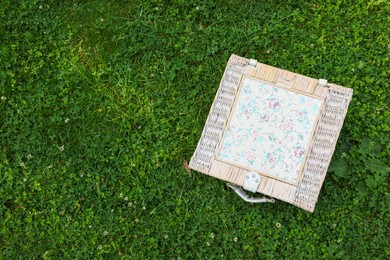 Photo of One picnic wicker basket on green grass, top view. Space for text