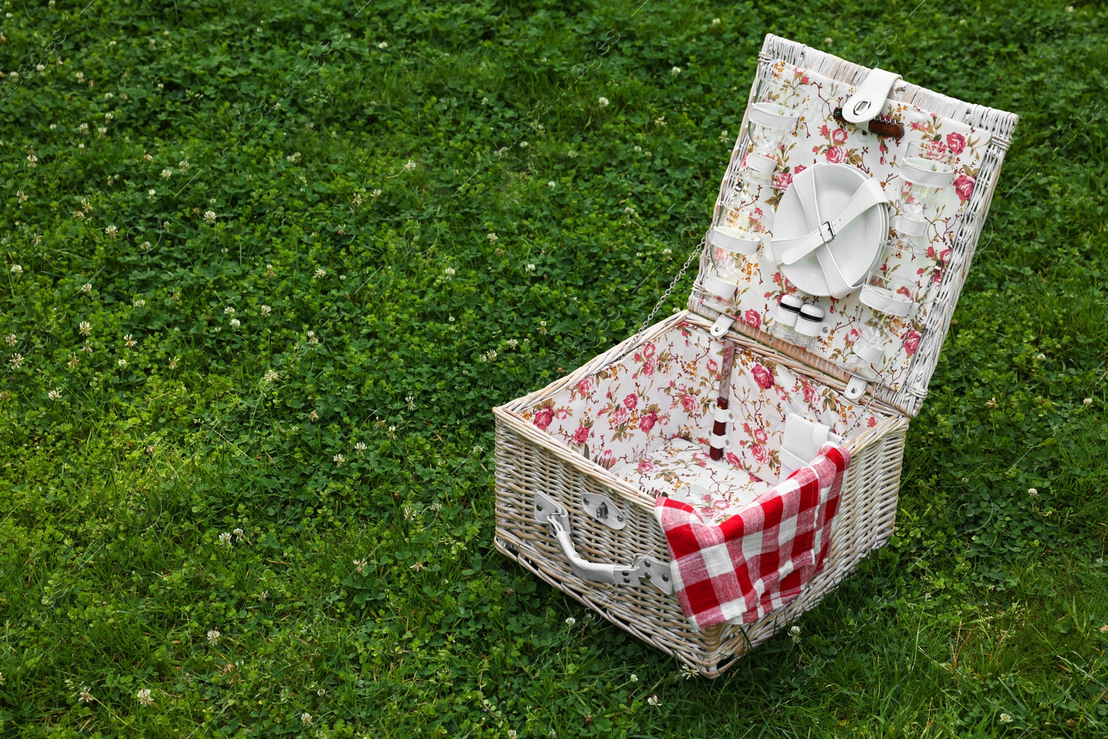 Photo of One picnic wicker basket with checkered napkin and tableware on green grass. Space for text