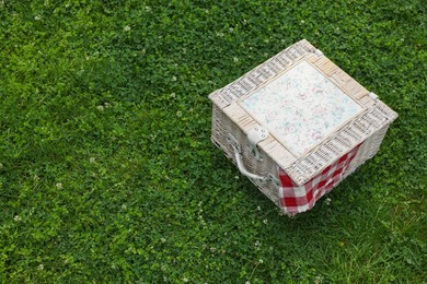 Photo of One picnic wicker basket with checkered napkin on green grass. Space for text