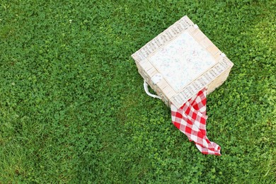 Photo of One picnic wicker basket with checkered napkin on green grass, above view. Space for text