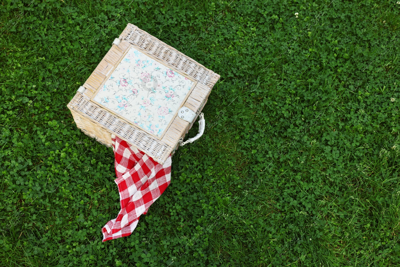 Photo of One picnic wicker basket with checkered napkin on green grass, above view. Space for text