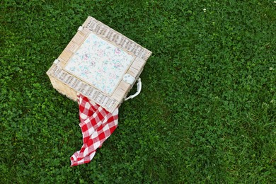 Photo of One picnic wicker basket with checkered napkin on green grass, above view. Space for text