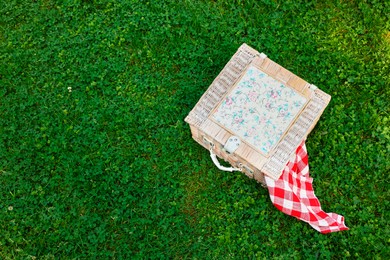 Photo of One picnic wicker basket with checkered napkin on green grass, above view. Space for text