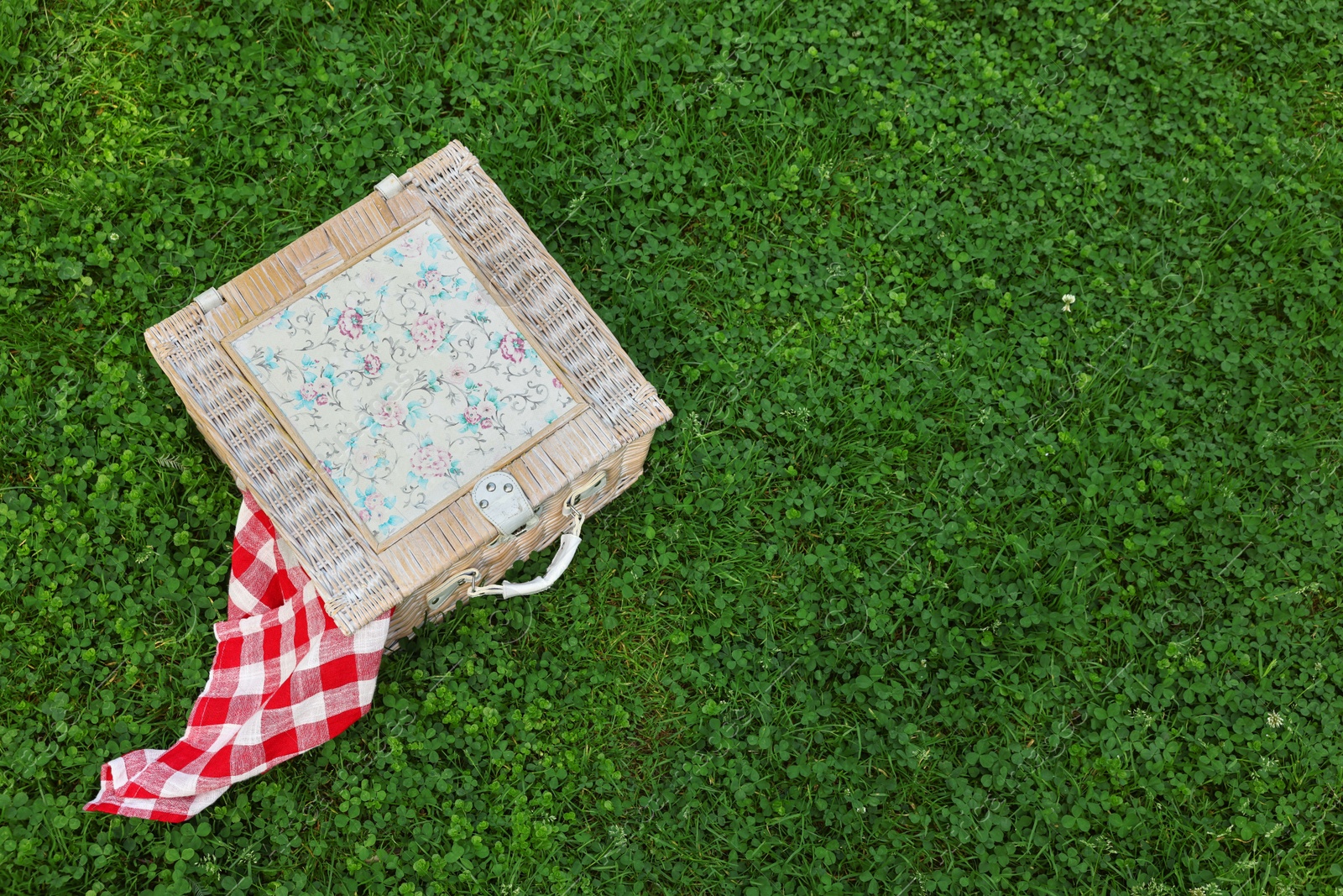 Photo of One picnic wicker basket with checkered napkin on green grass, above view. Space for text